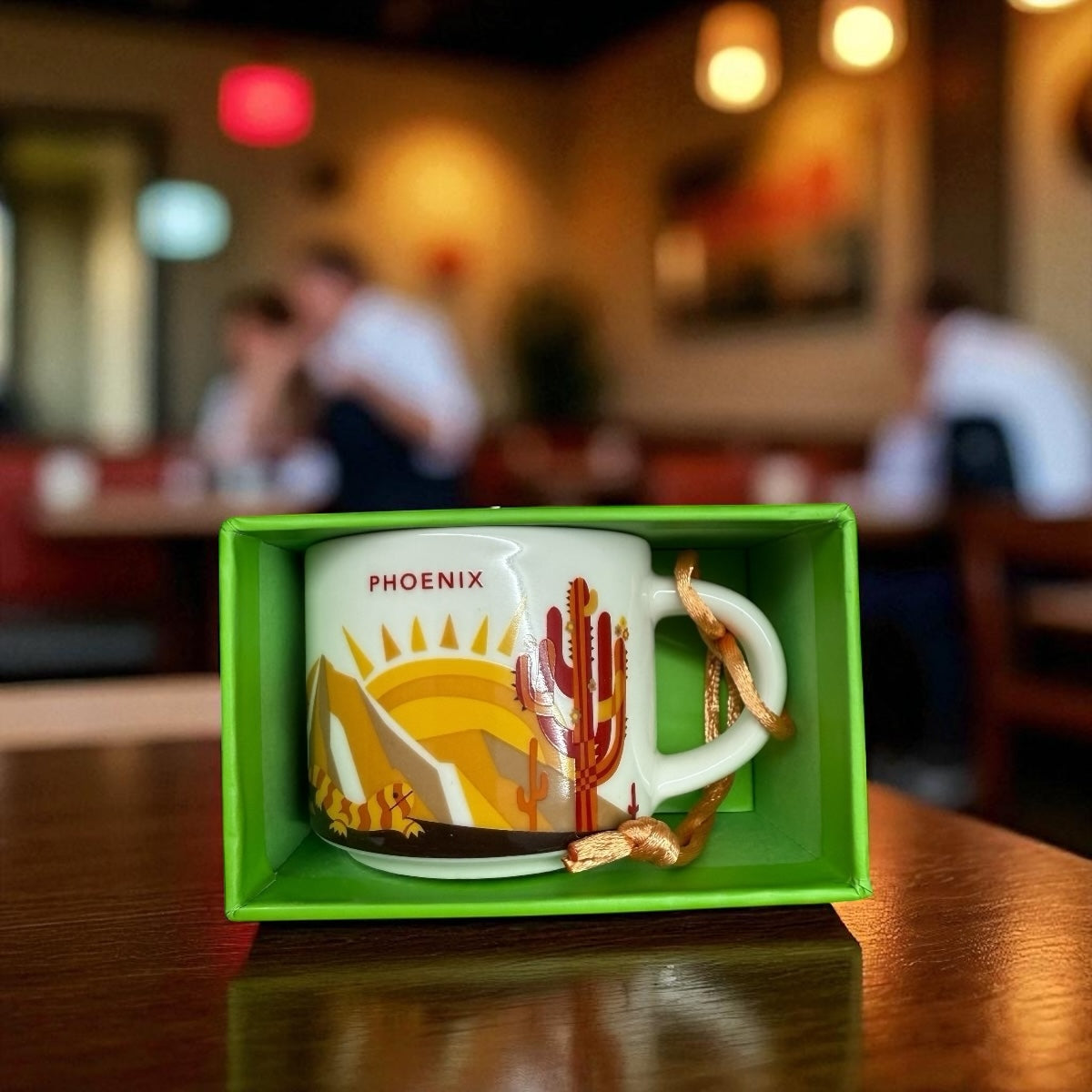 Ceramic mug with Phoenix design in a green box on a table in a restaurant setting