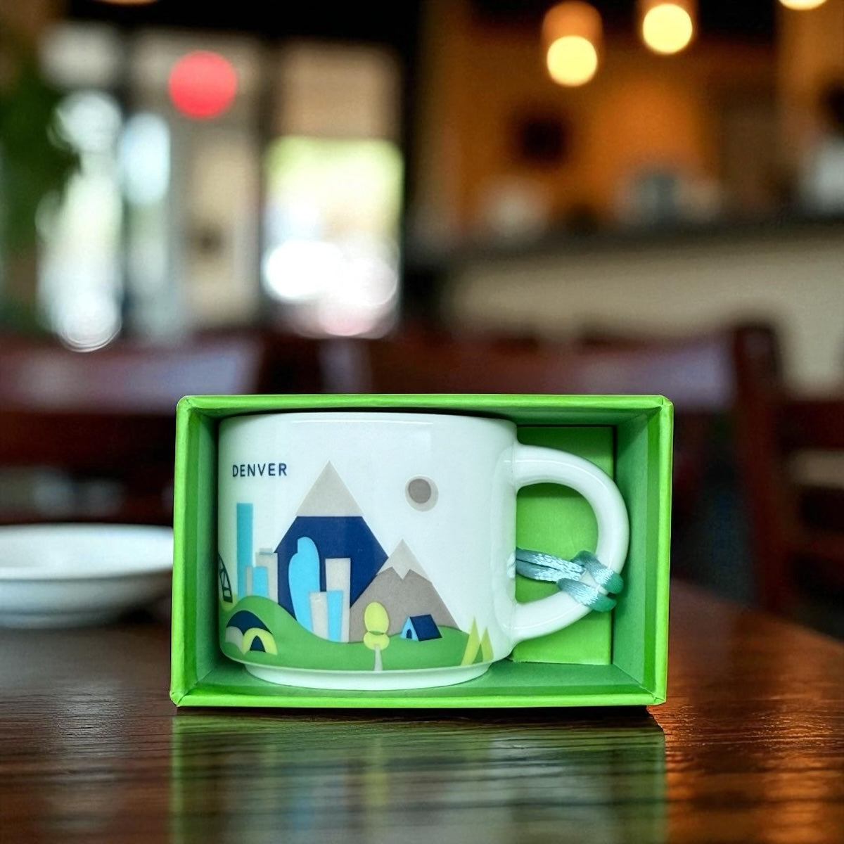 White mug with green and blue design in a green box on a wooden table.